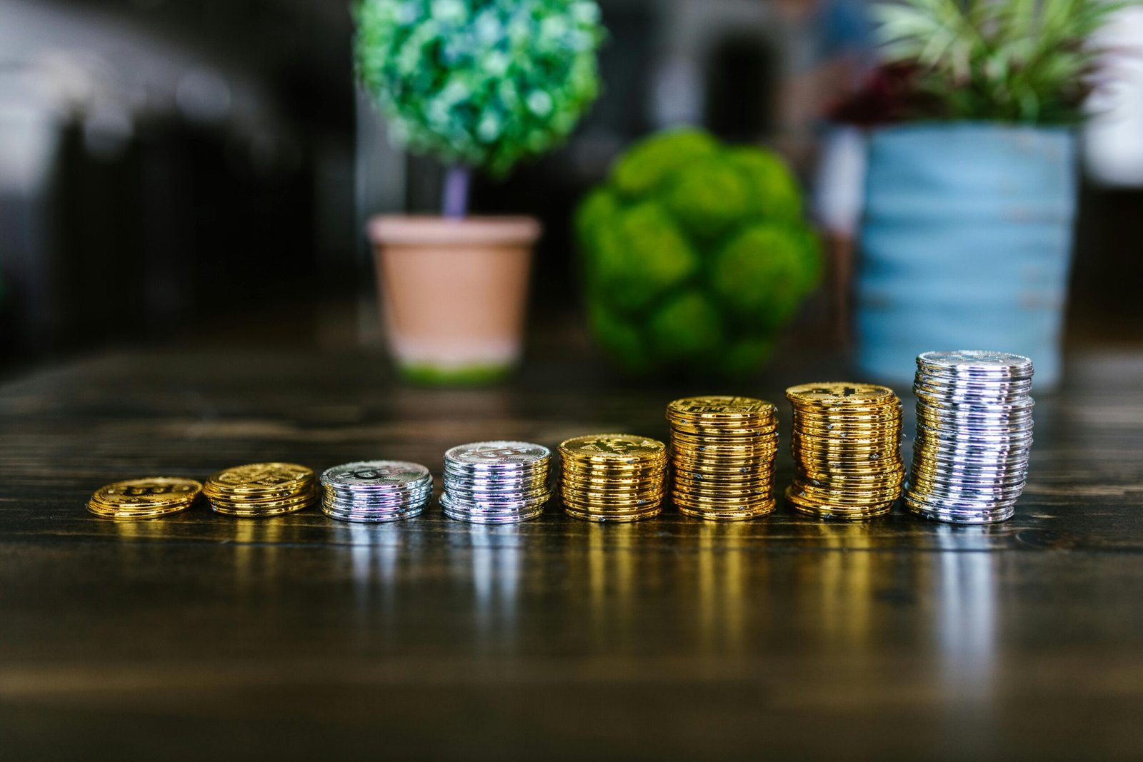 Close-up of stacked gold and silver bitcoins on a wooden table with plants in the background.